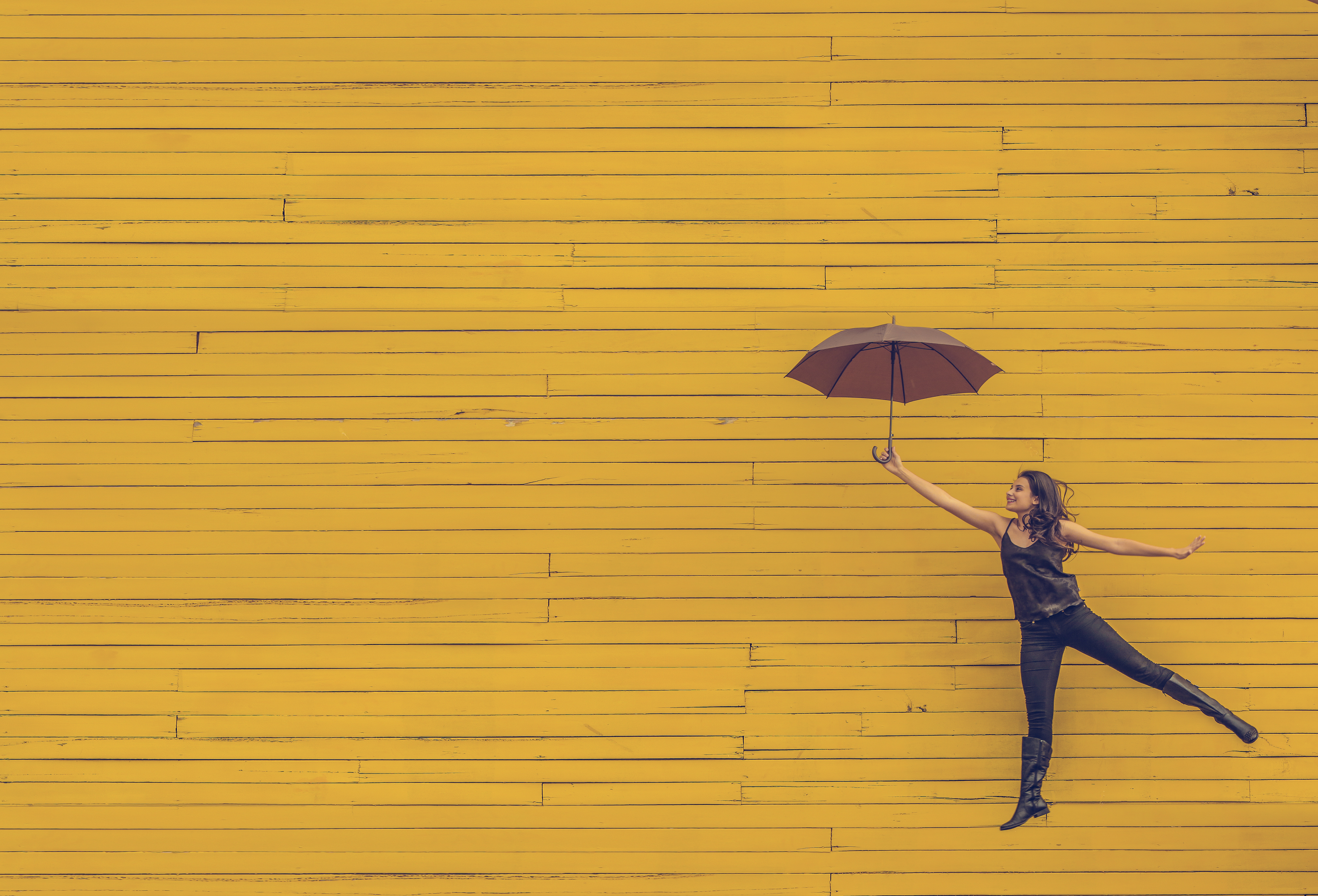 Women-learning-to-fly-with-umbrella-yellow-background